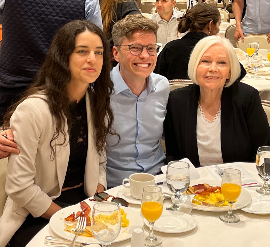 Ransom Wydner is seated in between his mother and female companion at the Justice Rising Breakfast, with breakfast plates of eggs, bacon and potatoes